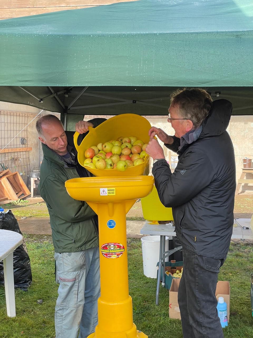 Volunteers loading harvested apples into a yellow apple crusher at a community orchard event