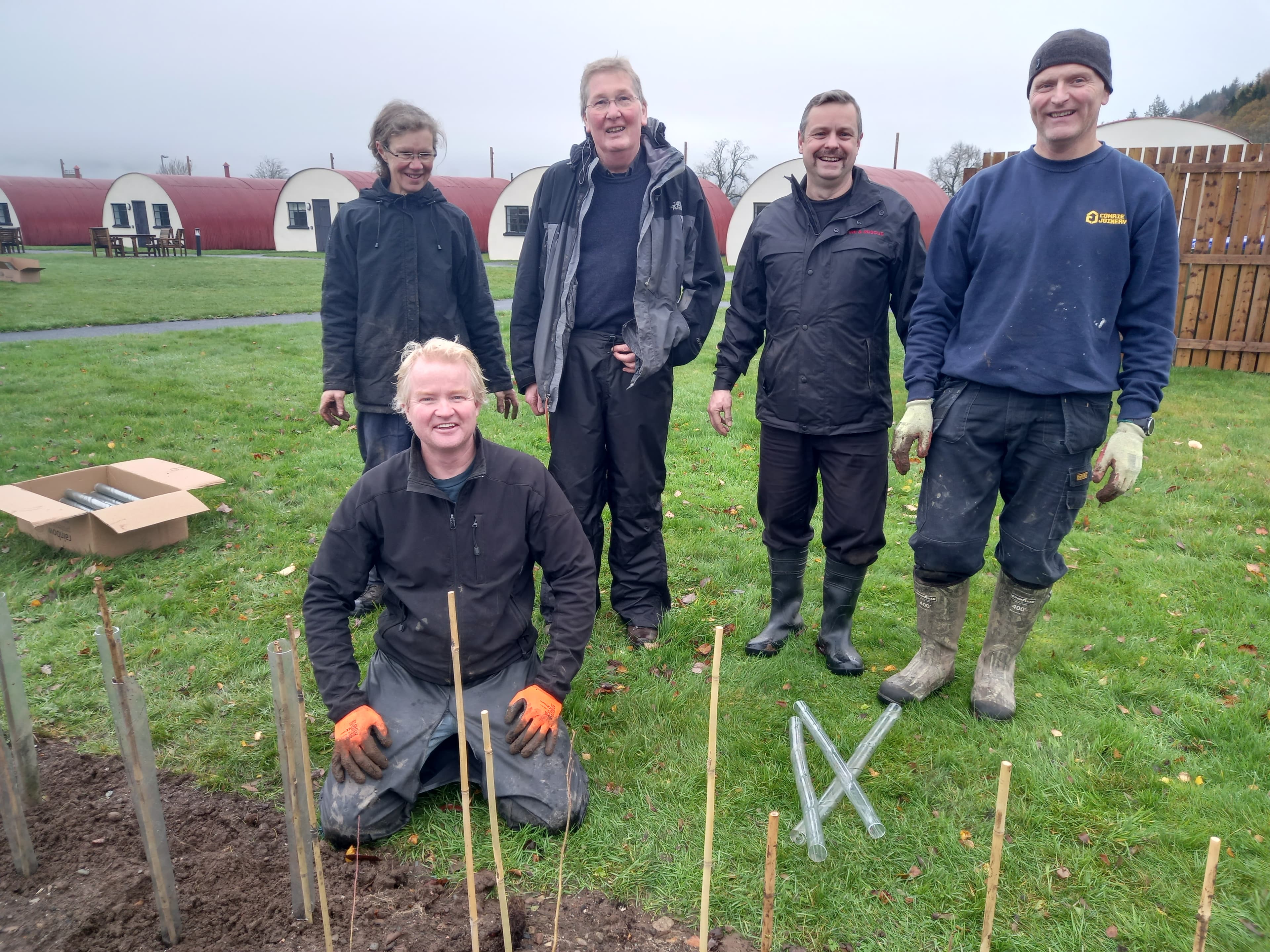 Volunteers planting young saplings at Cultybraggan Camp with Nissen huts in the background